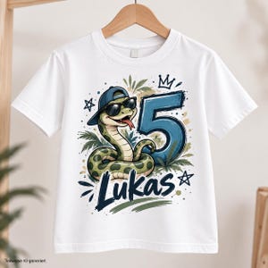 Könnte beinhalten: Ein weißes Kurzarm-T-Shirt mit einer Grafik einer grünen Schlange, die eine blaue Baseballkappe und eine schwarze Sonnenbrille trägt. Neben der Schlange befinden sich eine große blaue Zahl 5 und der Name Lukas in dunkelblauer Schrift.