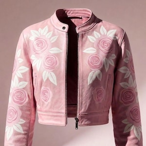 May include: A light pink leather jacket with a stand-up collar and a front zipper. The jacket is adorned with embroidered white and pink rose designs on the sleeves and front. The jacket's measurements are not visible in the image.