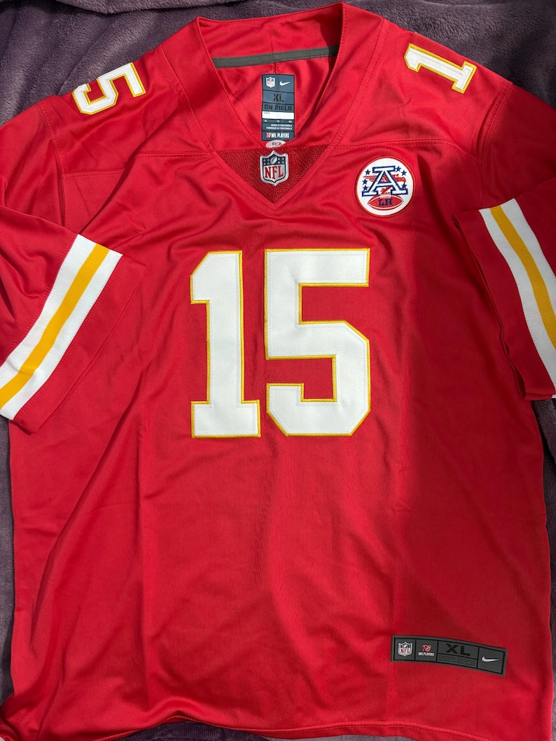 Puede incluir: Una camiseta de f&uacute;tbol roja talla XL con detalles blancos y amarillos. El n&uacute;mero 15 se muestra en blanco en la parte delantera, con el n&uacute;mero 5 en el hombro izquierdo. El logotipo de la NFL es visible en el cuello.