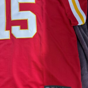 Puede incluir: Camiseta de f&uacute;tbol roja XL con el n&uacute;mero 15 en blanco con ribete amarillo. La camiseta tiene rayas blancas y amarillas en las mangas y los logotipos de la NFL y Nike.