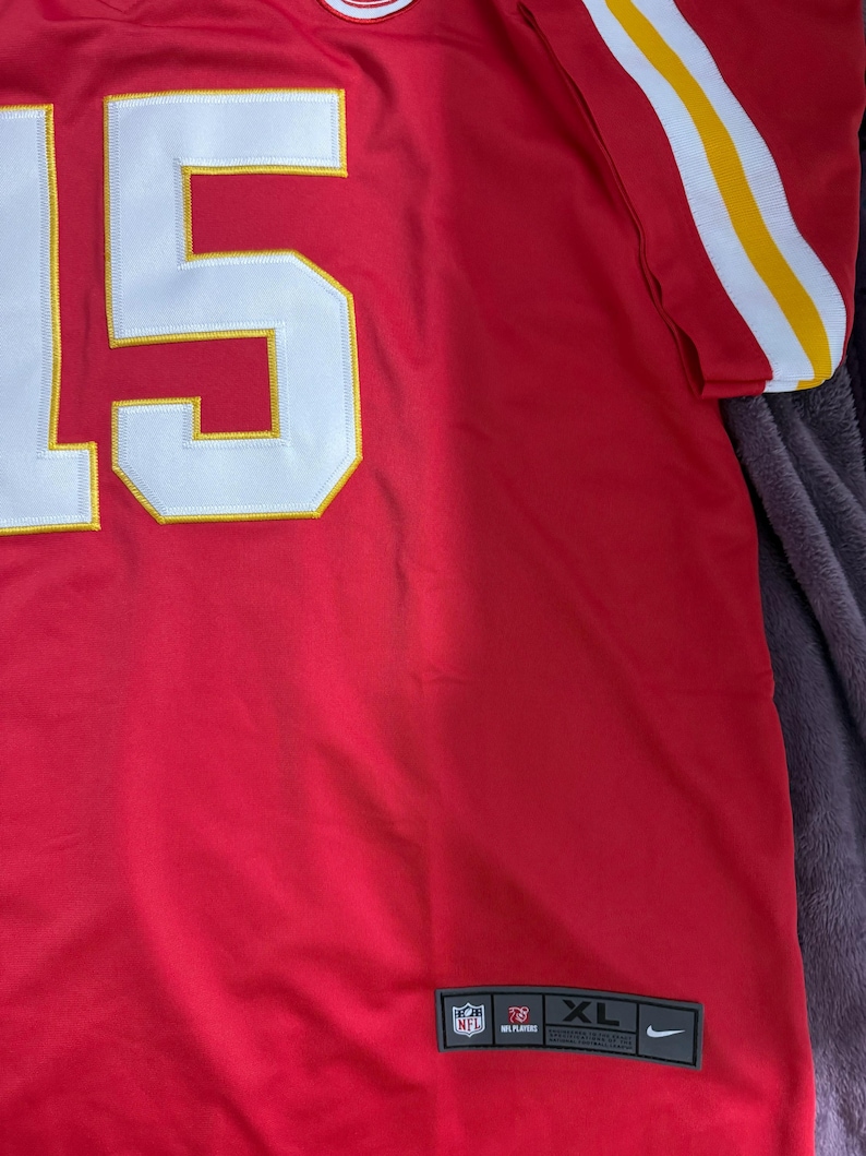 Puede incluir: Camiseta de f&uacute;tbol roja XL con el n&uacute;mero 15 en blanco con ribete amarillo. La camiseta tiene rayas blancas y amarillas en las mangas y los logotipos de la NFL y Nike.