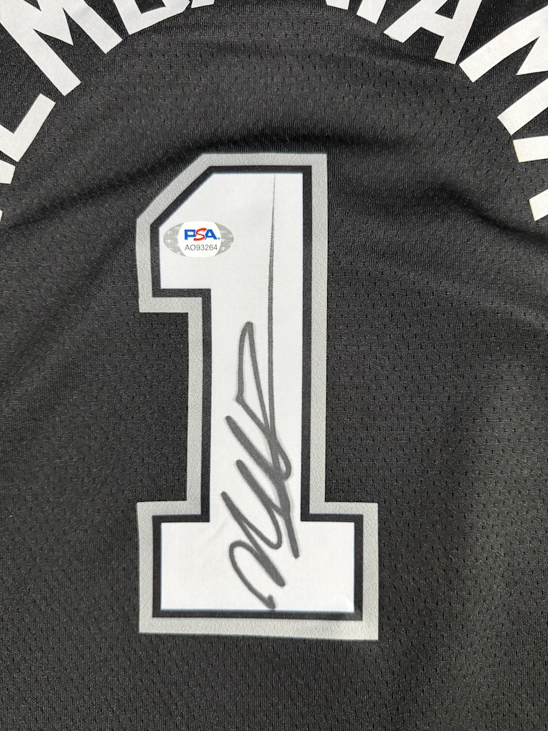 May include: A black mesh sports jersey featuring a large white number 1 with a grey and black outline. The number is signed in black ink and includes a PSA authentication sticker with the code AO93264. Partial white text is visible at the top.