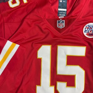 Puede incluir: Una camiseta de f&uacute;tbol americano de la NFL roja con el n&uacute;mero 15 en blanco con ribete amarillo. La camiseta tiene rayas blancas y amarillas en las mangas y un logotipo de la NFL en el pecho. La camiseta es talla XL.