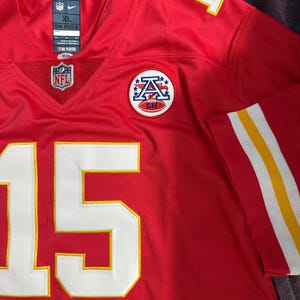 Puede incluir: Camiseta de f&uacute;tbol roja con detalles blancos y amarillos. El n&uacute;mero 15 en blanco con ribete amarillo en la parte delantera y el n&uacute;mero 1 en el hombro. Incluye logotipos de la NFL y del equipo. Talla XL.