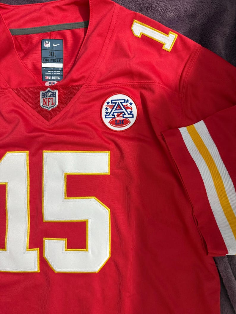 Puede incluir: Camiseta de f&uacute;tbol roja con detalles blancos y amarillos. El n&uacute;mero 15 en blanco con ribete amarillo en la parte delantera y el n&uacute;mero 1 en el hombro. Incluye logotipos de la NFL y del equipo. Talla XL.