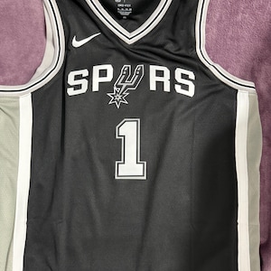 May include: A black San Antonio Spurs basketball jersey with white trim and the number 1 printed on the front. The jersey features the team name SPURS with a spur logo, a white Nike swoosh, and Dri-Fit branding on the inner collar area.