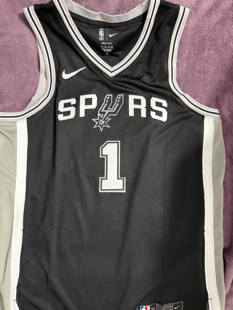 May include: A black San Antonio Spurs basketball jersey with white trim and the number 1 printed on the front. The jersey features the team name SPURS with a spur logo, a white Nike swoosh, and Dri-Fit branding on the inner collar area.