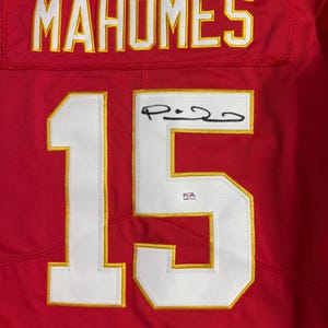 Puede incluir: Camiseta roja con el nombre "MAHOMES" en letras blancas y doradas en la parte superior. El n&uacute;mero "15" se muestra prominentemente en blanco con ribete dorado. Una firma es visible en el n&uacute;mero 15.