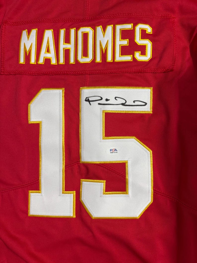 Puede incluir: Camiseta roja con el nombre "MAHOMES" en letras blancas y doradas en la parte superior. El n&uacute;mero "15" se muestra prominentemente en blanco con ribete dorado. Una firma es visible en el n&uacute;mero 15.