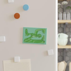 Könnte beinhalten: Ein rechteckiger Magnet mit einem grünen abstrakten Design auf hellgrünem Hintergrund. Das Design zeigt eine stilisierte menschliche Figur in Grüntönen. Der Magnet wird an einer weißen Kühlschranktür mit anderen Magneten angezeigt.