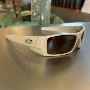 May include: Tan-colored sunglasses with dark brown lenses. The sunglasses have a rectangular frame with a silver emblem on the side. The design is sleek and modern, suitable for outdoor activities.