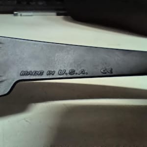 May include: A dark gray, elongated object with the text "MADE IN U.S.A." and "CE" embossed on its surface. The object has a pointed end and appears to be a tool or part of a larger device.