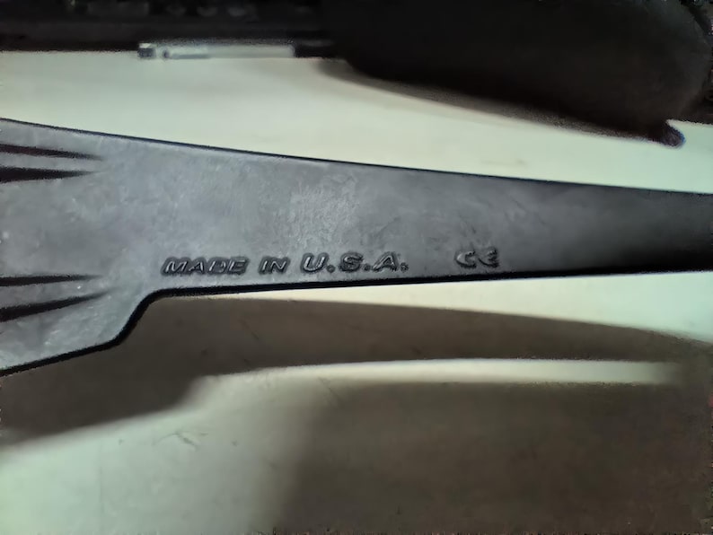 May include: A dark gray, elongated object with the text "MADE IN U.S.A." and "CE" embossed on its surface. The object has a pointed end and appears to be a tool or part of a larger device.