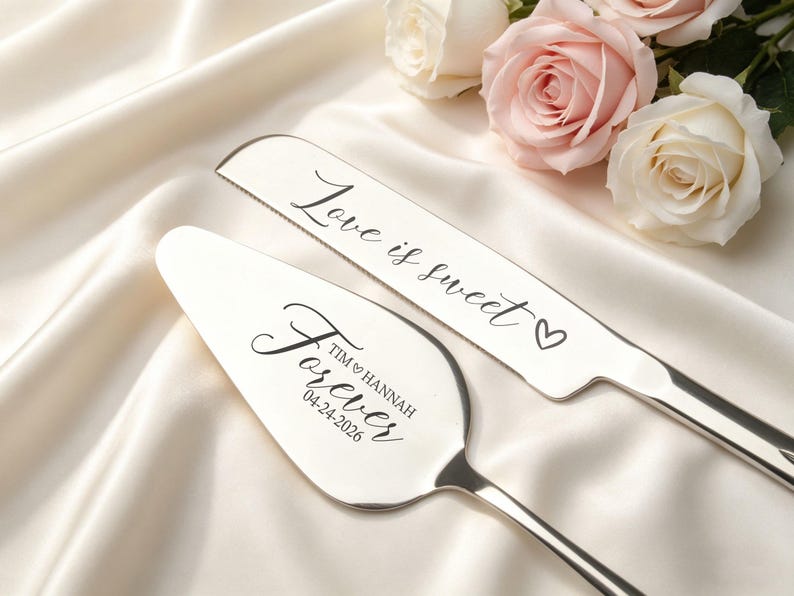 May include: Silver cake knife and server set with the words "Love is sweet" and "Forever" engraved. The server is personalized with a name and date. The set is displayed on a white satin surface with roses.