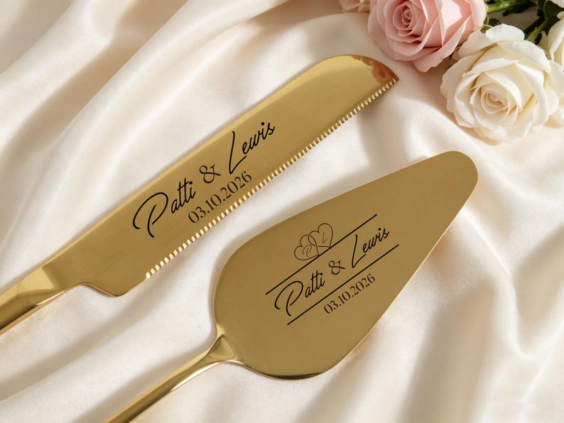May include: Gold-colored wedding cake knife and server set. The knife has a serrated edge and the server is spade-shaped. Both are engraved with "Patti & Lewis" and the date 03.10.2026. The set is displayed on a white satin surface.
