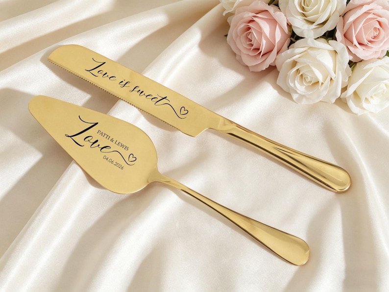 May include: Gold-colored cake knife and server set with the words "Love is sweet" and "Love" inscribed. The server is personalized with names and a date. The set is displayed on a white satin surface, with a bouquet of roses in the background.