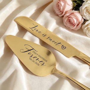 May include: A gold-colored cake knife and server set. The knife has the words "Love is sweet" and a heart etched on the blade. The server is engraved with "Forever" and a date. Roses in the background.