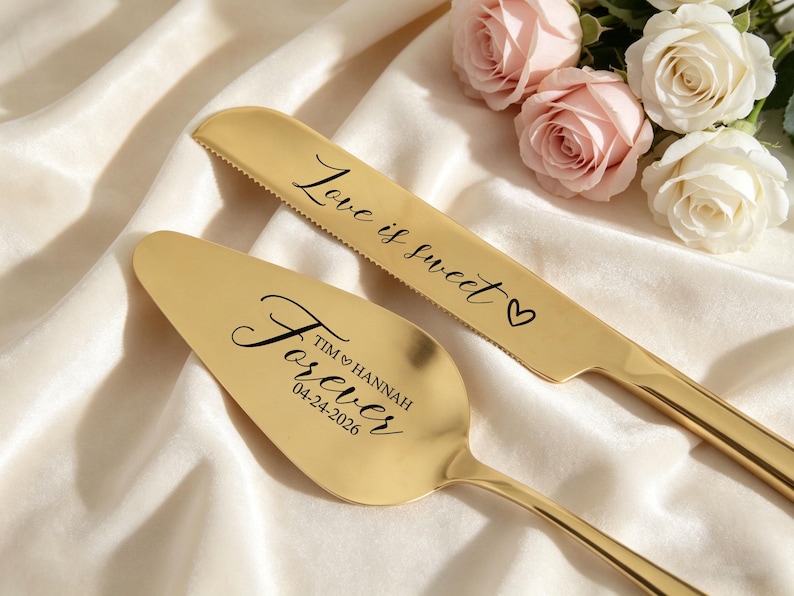 May include: A gold-colored cake knife and server set. The knife has the words "Love is sweet" and a heart etched on the blade. The server is engraved with "Forever" and a date. Roses in the background.