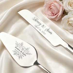 May include: A silver cake knife and server set. The knife is engraved with "Avery & Sam" and "April 26, 2025". The server is engraved with "Avery & Sam" and "November 26, 2025" along with floral designs. The set is displayed on a white satin surface.