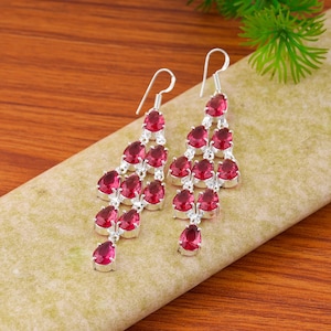 May include: A pair of silver chandelier earrings featuring multiple teardrop-shaped red gemstones arranged in a cascading pattern. Each earring is suspended from a silver hook and showcases several faceted red stones set in polished silver metal.