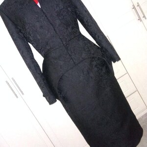 May include: A black, long-sleeved dress with a fitted bodice and a flared skirt. The dress has a textured, floral pattern and a high neckline.