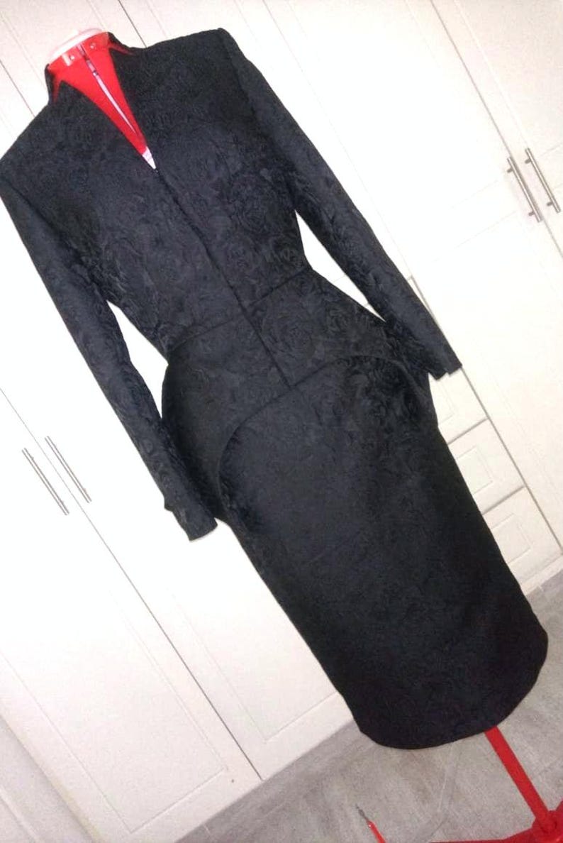 May include: A black, long-sleeved dress with a fitted bodice and a flared skirt. The dress has a textured, floral pattern and a high neckline.