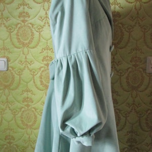 May include: A light blue coat with a large collar and long sleeves. The sleeves have a gathered detail at the elbow.