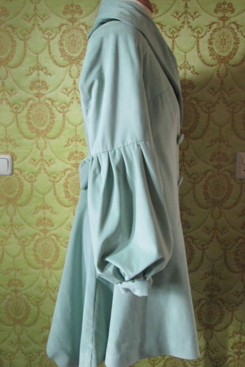 May include: A light blue coat with a large collar and long sleeves. The sleeves have a gathered detail at the elbow.