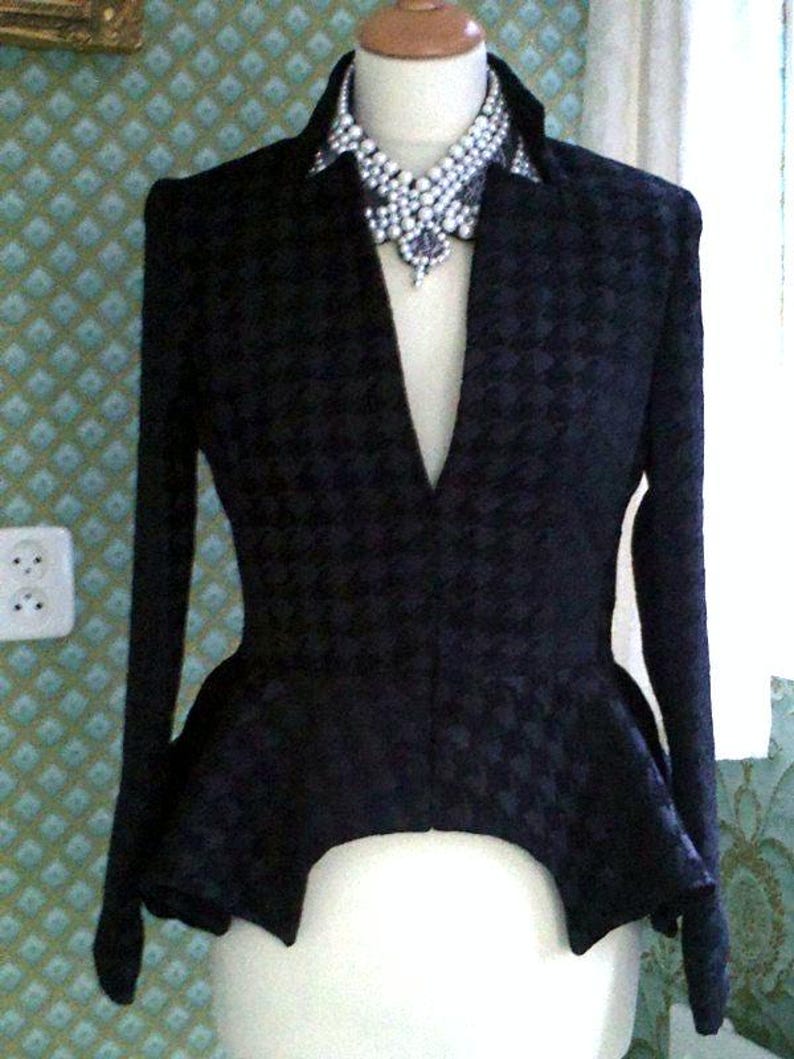 May include: A black blazer with a peplum hem and a pointed collar. The blazer has a floral pattern and is worn with a large pearl necklace.