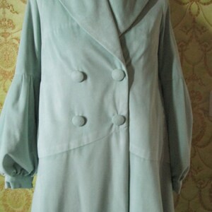 May include: A light blue double-breasted coat with a large collar and long sleeves. The coat has four buttons down the front.