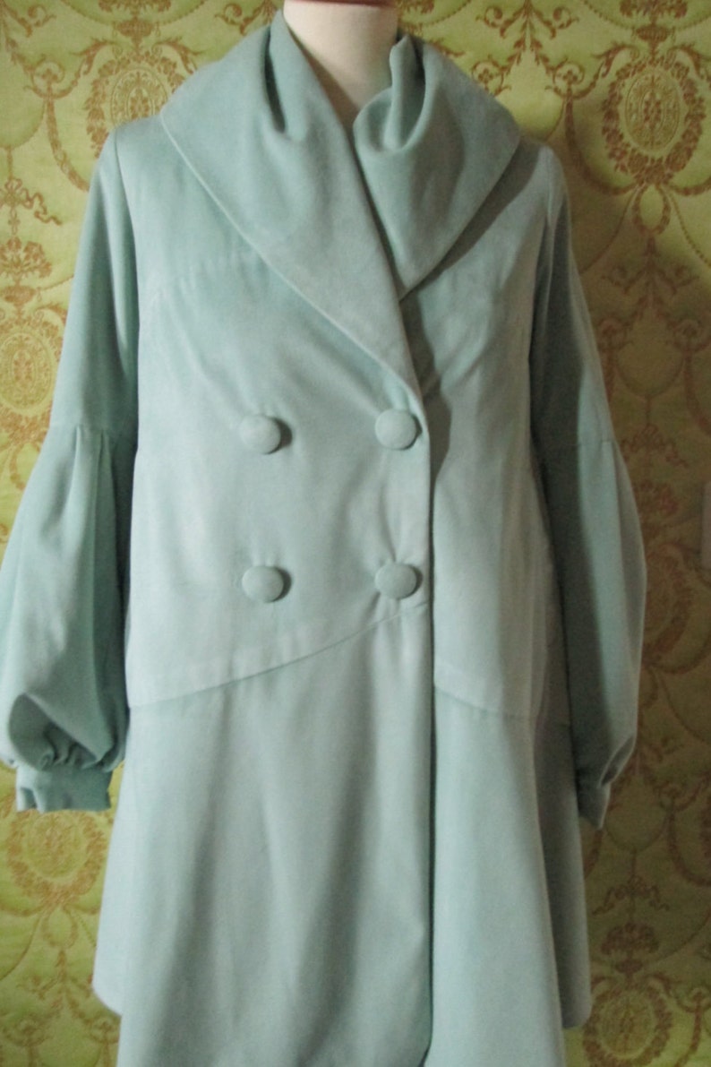 May include: A light blue double-breasted coat with a large collar and long sleeves. The coat has four buttons down the front.