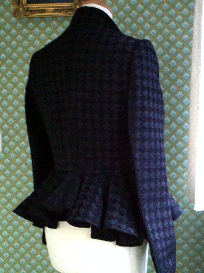 May include: A black and blue patterned jacket with a ruffled hem. The jacket has a high collar and a fitted silhouette.