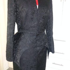 May include: A black, long-sleeved dress with a floral pattern. The dress has a fitted bodice and a flared skirt. The dress is cinched at the waist with a belt.