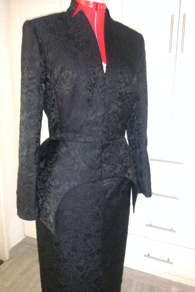 May include: A black, long-sleeved dress with a floral pattern. The dress has a fitted bodice and a flared skirt. The dress is cinched at the waist with a belt.