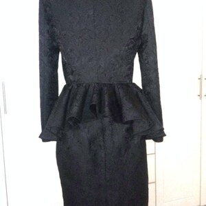 May include: A black dress with a high neck and a ruffled peplum. The dress is made of a textured fabric and has long sleeves.