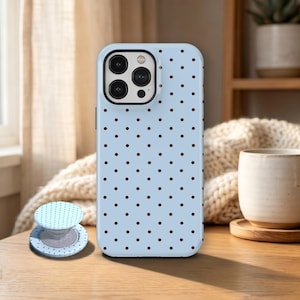 May include: A light blue phone case with a polka dot pattern and a matching phone grip. The phone case is on a wooden table. The phone case has a black camera lens area.