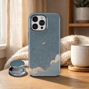 May include: A blue smartphone case and a matching circular phone grip featuring a night sky design with a small crescent moon and soft, fluffy white clouds at the bottom. The case has a cutout for a triple-lens camera system on the back.