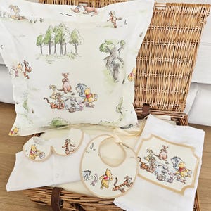 May include: A wicker basket contains a Winnie the Pooh themed baby gift set. The set includes a pillowcase, a onesie with a Peter Pan collar, a bib, and a small blanket. Each item features illustrations of Winnie the Pooh and friends in a whimsical outdoor scene.