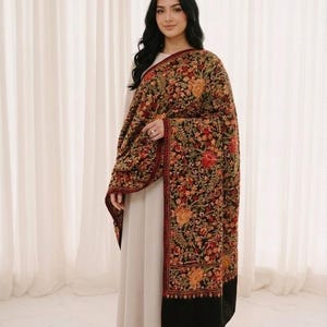 Puede incluir: Una mujer con un vestido beige y un chal. El chal es oscuro con un estampado floral en rojo, naranja y verde. El chal tiene un borde negro y un ribete rojo.