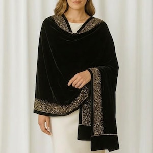 Puede incluir: Un chal de terciopelo negro con ribete de cuentas doradas. El chal est&aacute; drapeado sobre un vestido color crema. El ribete dorado est&aacute; a lo largo de los bordes del chal y alrededor del escote. La mujer lleva un collar de oro.