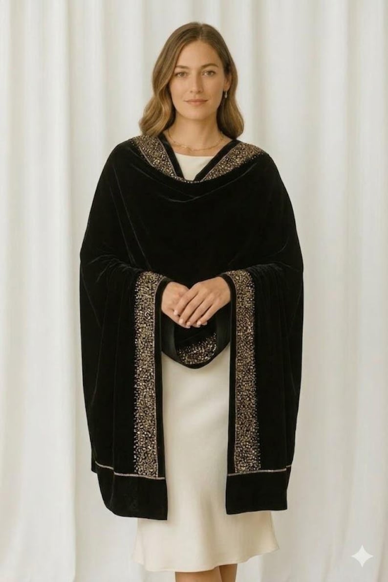 Puede incluir: Un chal de terciopelo negro con ribete de cuentas doradas. El chal est&aacute; drapeado sobre un vestido blanco. El ribete recorre los bordes del chal y alrededor del escote. Un accesorio lujoso.