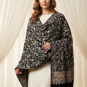 May include: A black shawl with a detailed floral and bird pattern in shades of pink, yellow, and green. The shawl is draped over a white dress. The shawl has a black border.