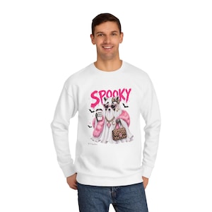 Peut inclure: Un sweat-shirt blanc à col rond avec une impression graphique représentant un fantôme portant des lunettes de soleil roses, une étole en fourrure rose et des chaînes dorées, tenant un café marqué 'more boo please' et un sac à motif léopard.