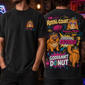 May include: A black t-shirt featuring a small graphic of a cat wearing a crown and sunglasses on the front left chest. The back displays a large, colorful graphic with three orange cats, text reading The Royal Court of Princess Donut, This is an Outrage, and Goddamnit Donut, along with a gold trophy and a donut illustration.