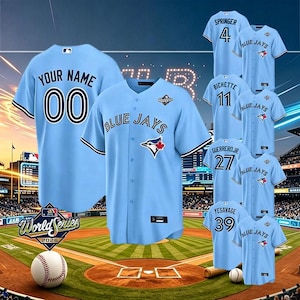 Puede incluir: Camisetas de béisbol azul claro con el texto "Blue Jays" y nombres y números de jugadores. Una camiseta tiene "Your Name" y el número "00". También se ven una pelota de béisbol y las palabras "World Series 2026".