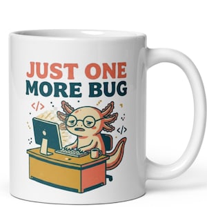 Può includere: Una tazza in ceramica bianca con la grafica di un axolotl con occhiali, seduto a una scrivania con un computer e una tastiera. Il testo sopra l'illustrazione recita JUST ONE MORE BUG in arancione e blu scuro, con simboli di codice ai lati.