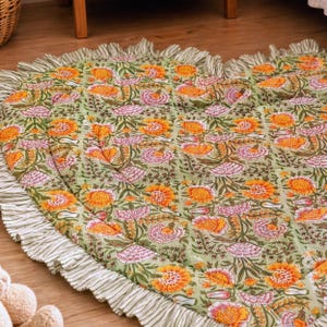 Peut inclure: Un tapis matelassé en forme de cœur avec un fond vert clair et un motif floral répétitif orange et rose. Les bords sont finis avec une bordure à volants rayée blanche et verte, créant une finition texturée tout autour du tapis.