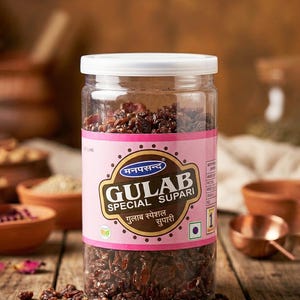May include: A clear plastic jar with a white lid filled with dark brown Gulab Supari. The jar has a pink label with gold lettering and the words "GULAB SPECIAL SUPARI". Scattered Supari pieces are on a wooden surface.