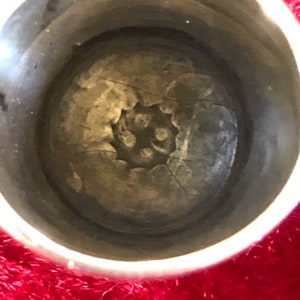 May include: Close-up of a silver thimble interior. The thimble's interior features a textured, circular design with a series of small, raised dots at the center. The thimble's rim is smooth and reflective, contrasting with the textured interior.