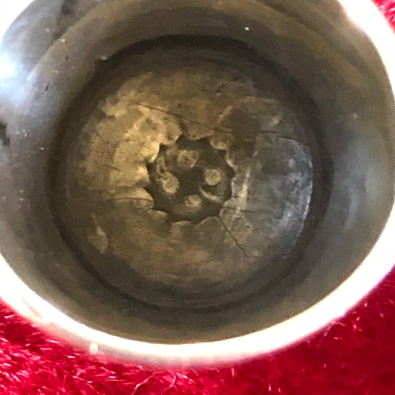 May include: Close-up of a silver thimble interior. The thimble's interior features a textured, circular design with a series of small, raised dots at the center. The thimble's rim is smooth and reflective, contrasting with the textured interior.